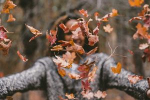 Woman throwing leaves in the air in the forest
