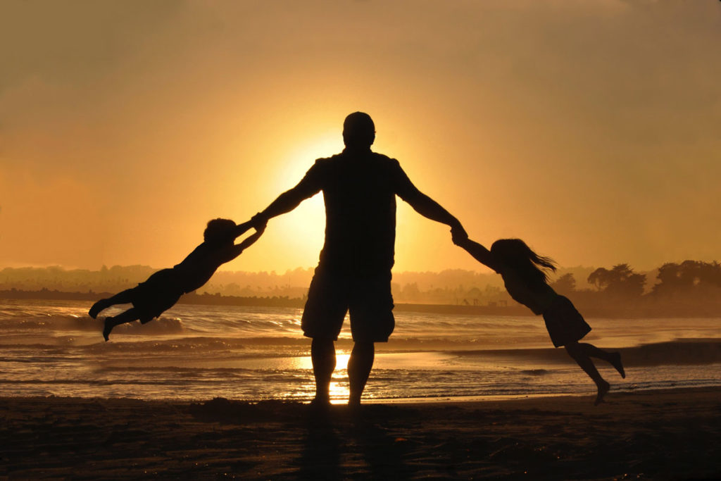 Perfektes Familienfoto: Vater und Kinder spielend am Strand im Sonnenuntergang