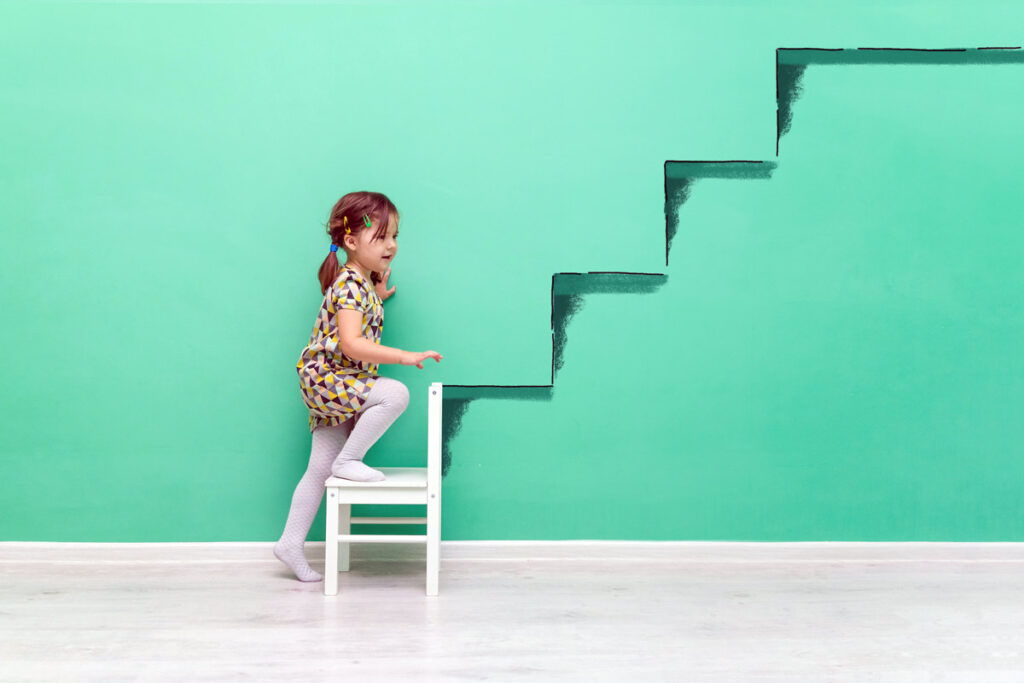 A little girl pretends to climb stairs painted on green wall