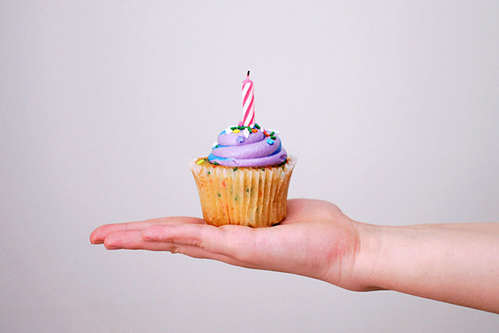 hand holds a cupcake with a candle on top