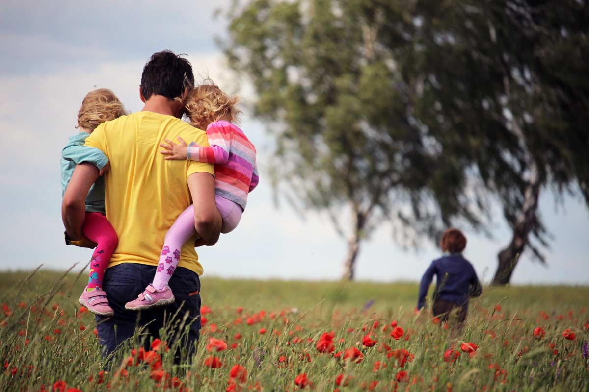 Dad hold two kids in a field