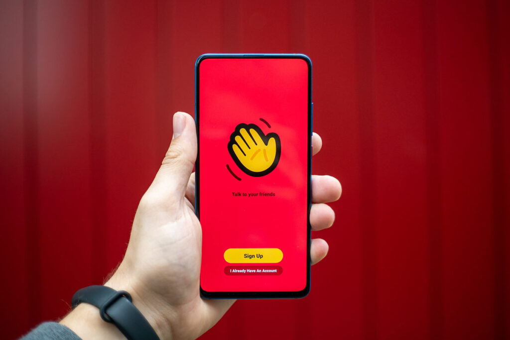 A hand holds a phone with the House Party app for staying connected