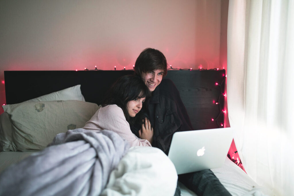 This couple lying in bed show how to stay in touch with a video call
