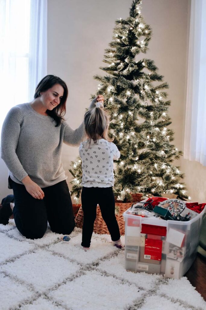 Mother helps toddler decorate the tree to get in the festive spirit