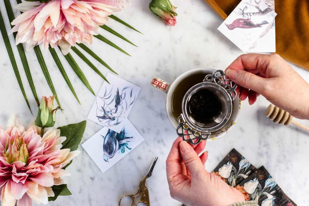 A person holds coffee in this one of our flat lay ideas surrounded by flowers and paintings