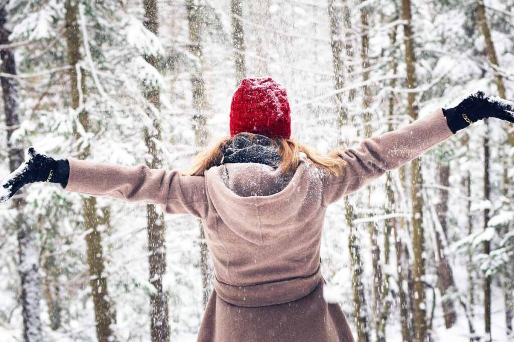 Eine Frau steht glücklich mit Armen breit im Schnee