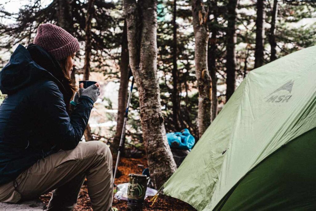 Eine Frau trinkt Tee neben ihre Zelt im Wald