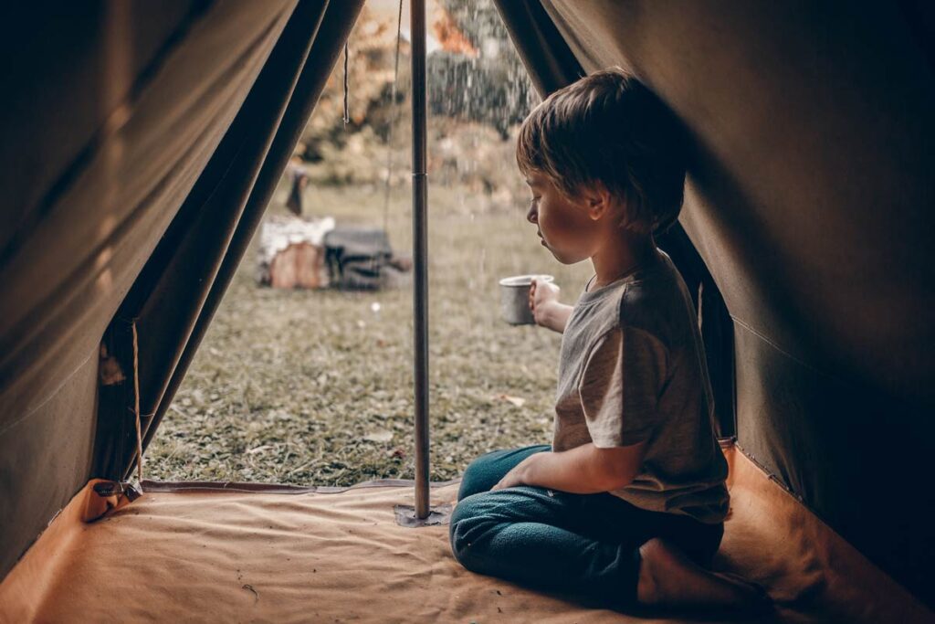 Ein Kind schaut die Regen an in seinen Zelt