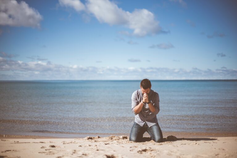 A man kneels in prayer for Ramadan on a beach showing humility.