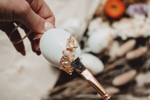 A paintbrush paints the gold leaf delicately on to the prepped Easter egg