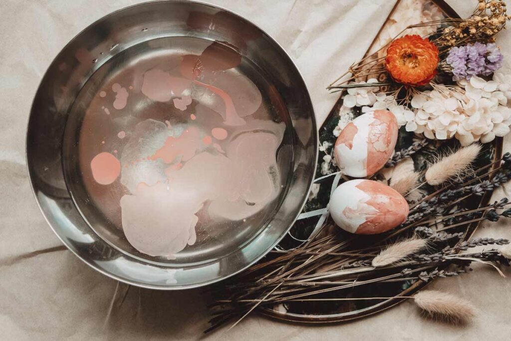 Nail polish floats in a bowl of water with 2 newly marbled eggs drying next to it