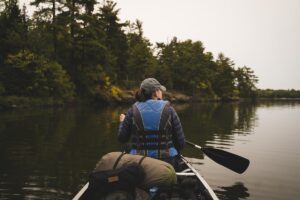 A woman sits with her camping gear in a rowing boat on the water.