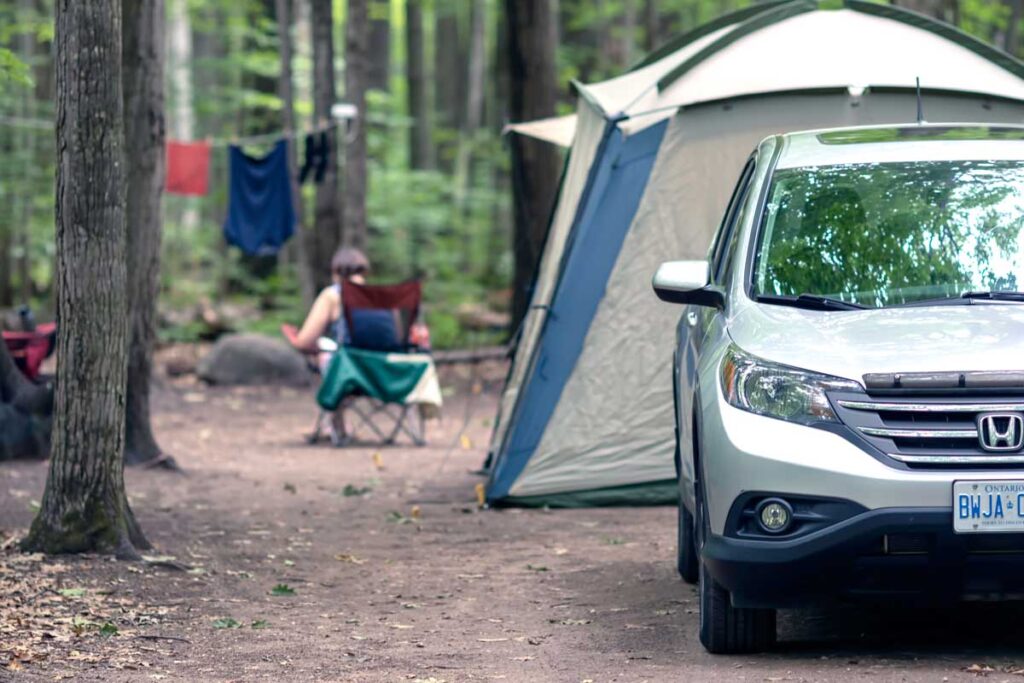 A car parked in front of a tent on a campsite in the forest