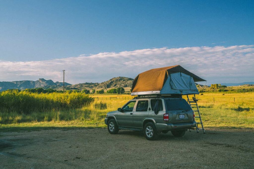 This type of camping involves a tent on top of the car, here seen at the end of a green landscape.