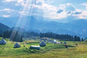 A group of yurts in the sunshine with the mountains in the background.