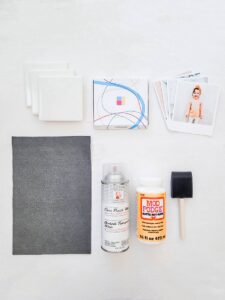 The materials for a DIY photo coaster on a white background: grey felt, a pack of prints, a photo, Mod Podge, a brush, spay and the ceramic tiles.