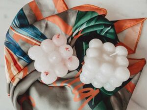 Two homemade white bubble candles lie on a orange and green material.