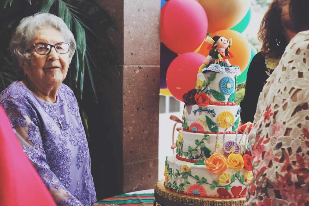 Eine alte Frau steht neben ein riesige Geburtstagskuchen, um ihrem Meilenstein Geburtstag zu feiern