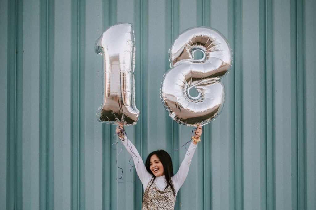 Eine 18-Jährige Frau haltet Nummer-Luftballoons hoch am ihrem Meilenstein Geburtstag
