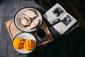 A bird's eye view of a brunch with egg and mango on two plates, a cup of coffee and a book with glasses on top.
