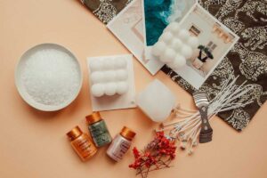 A flat laying on an apricot background showign the materials needed to make a bubble candle from scratch - 3 colour pigment bottles, 2 ready candles, wax, dried flowers and the wicks. Int he corner, photo prints.