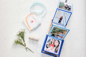 DIY accordion photo box next to a MyPostcard box of photos, flowers and some string.