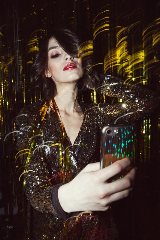 A woman in an evening outfit takes a photo from below in a dark room in a glittery dress.