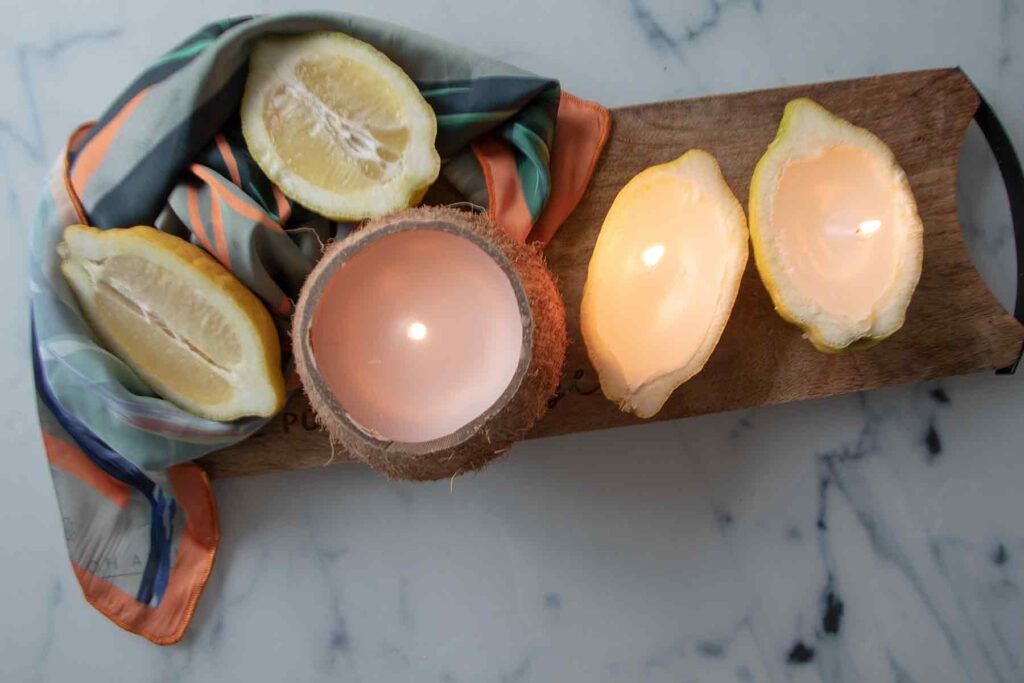 The DIY cocounut and lemon shell candles are lit on a wooden board next to two lemon halves