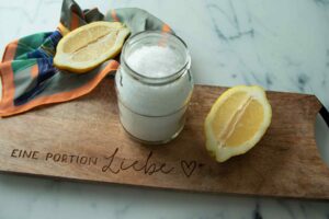Wax in a glass jar and two lemon halves on a wooden board
