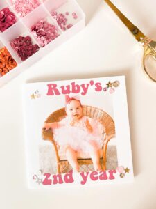 A box of sequins and sparkles next to the DIY photo yearbook.