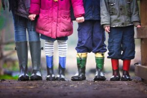 Four kids in a row wearing rain gear seen from shoulders to welly boots