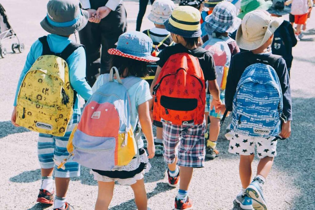 A group of children head to their first day of school, each wearing a bright backpack