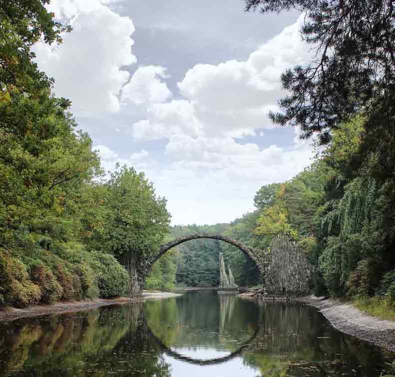 Brücke über einem See, wird im See gespiegelt. Umgeben von Wald.
