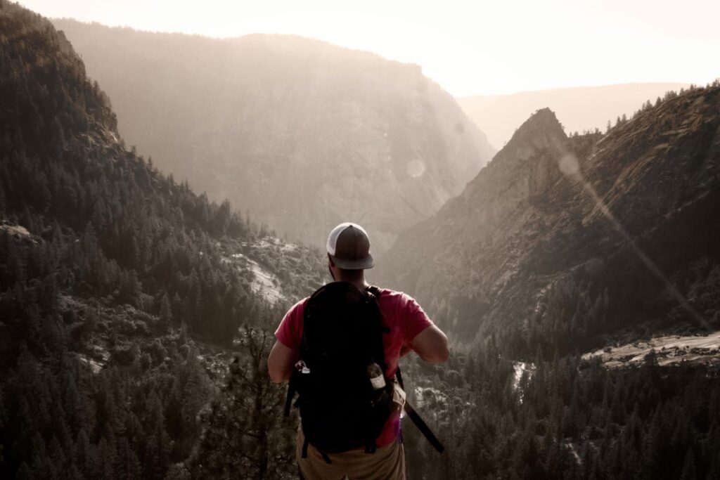 A man with a backpack faces the mountainous scenery to check one of the best hiking apps on his phone