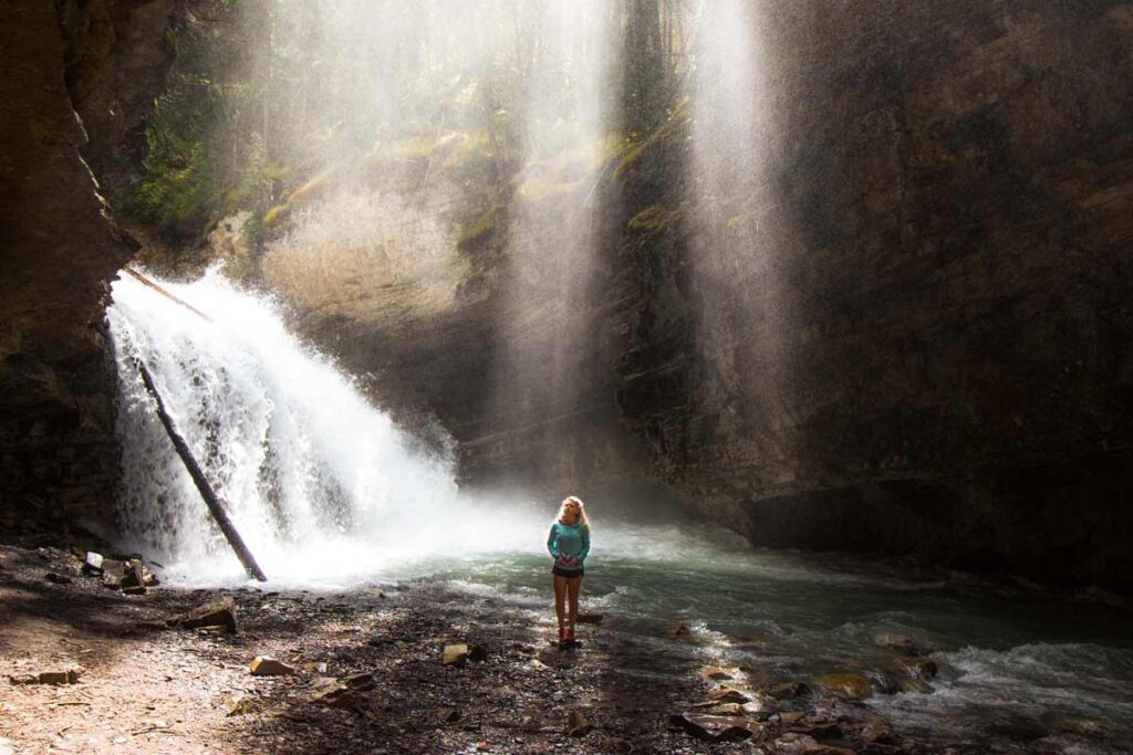 With light cascading down next to a waterfall a woman poses on her hike