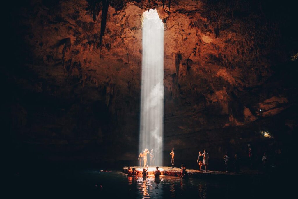 A stream of light entering a swimming cave onto the people swimming and standing below