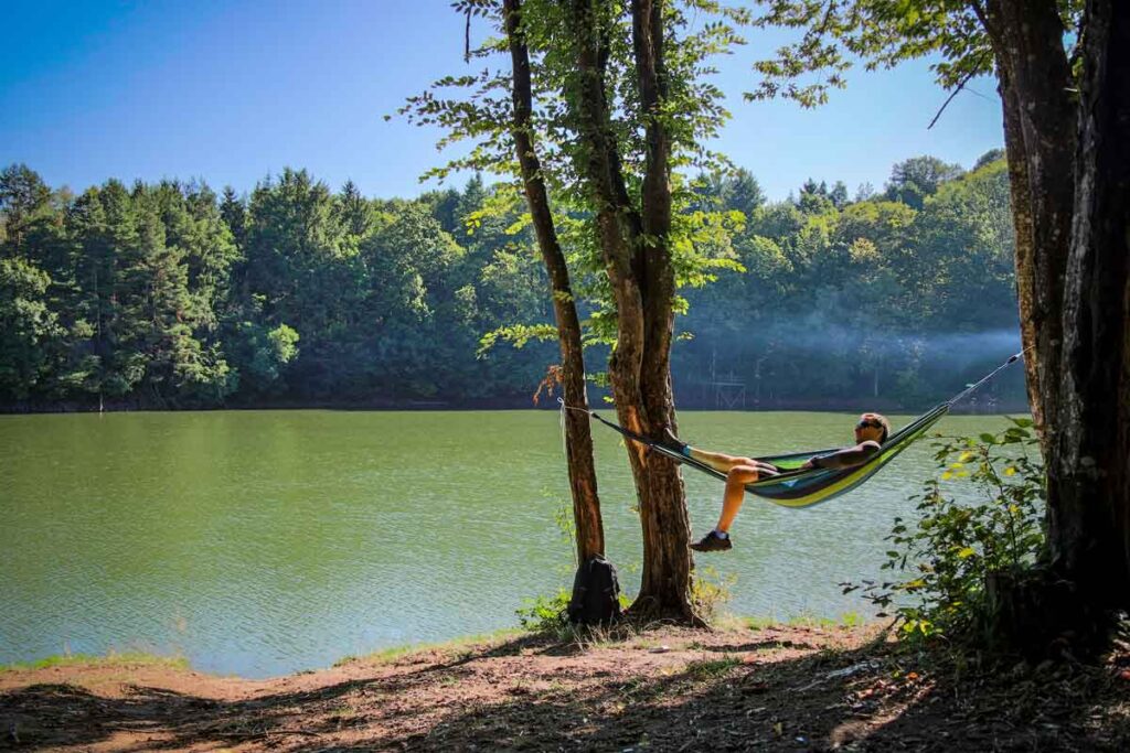 A travel hammock sat in front of the water with a man reflecting on why traveling is important.