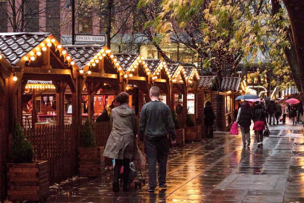A line of Christmas huts at one of the Manchester Christmas markets, one of the best in Europe., as a couple walk by hand in hand.