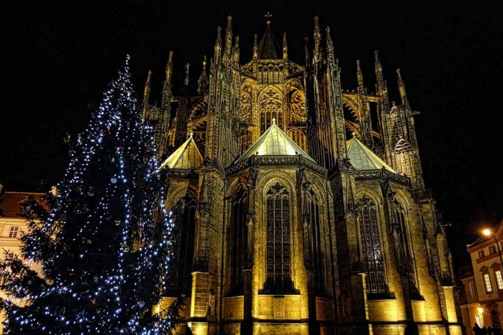 Winter and a lit Christmas tree in front of the Prague Cathedral at night.