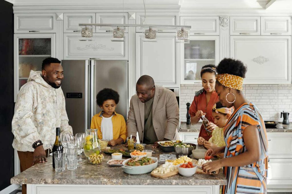 A family gather around a kitchen island covered in food chatting and laughing during Thanksgiving