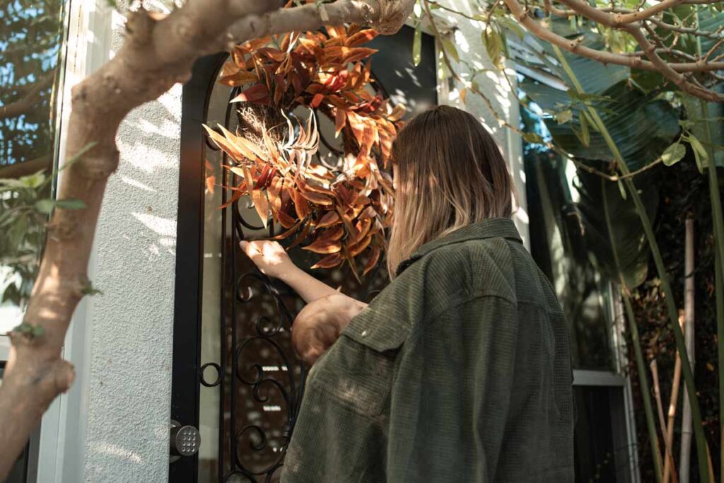 A woman knocks at the door of a house with a Autumnal wreath, ready to celebrate Thanksgiving differently with alternative ideas