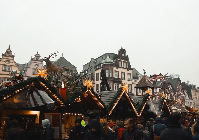 Menschen vor den Hütten des Weihnachtsmarktes von Trier. 
