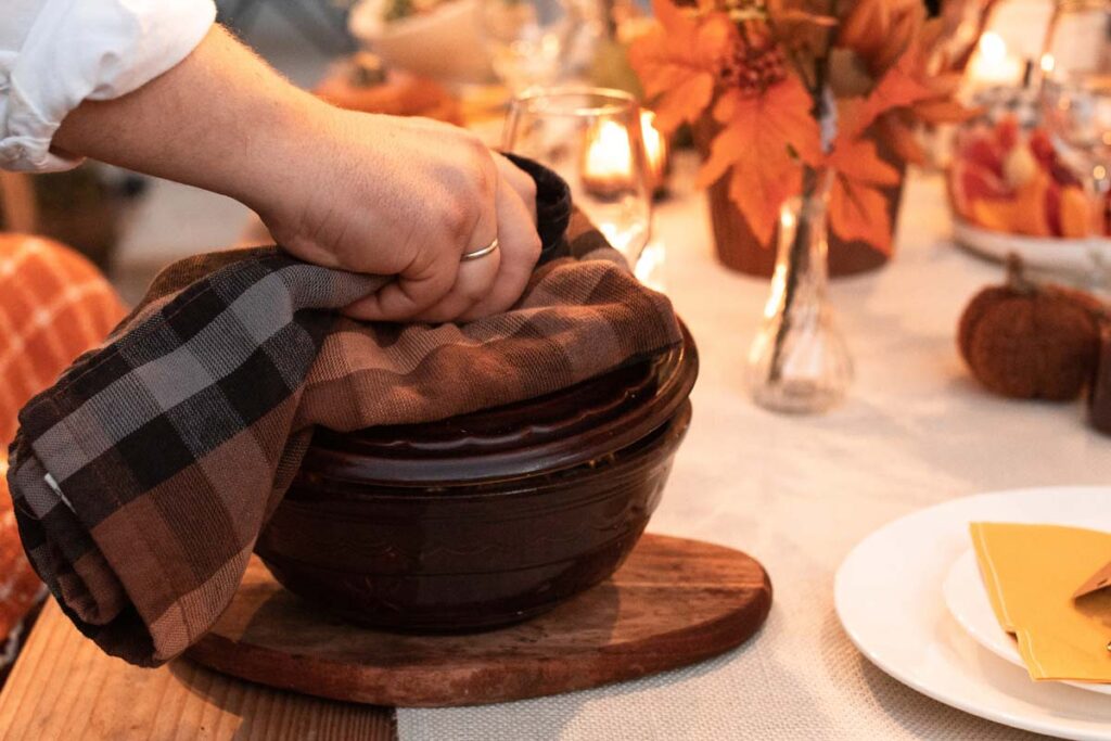 A close up of a casserole dish being placed onto a fall-decorated table