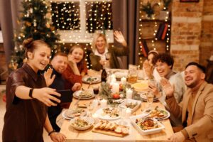A group of friends take a selfie together around a table filled with Thanksgiving foods, during Friendsgiving