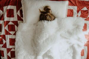A woman lies in bed with her face covered with the douvet