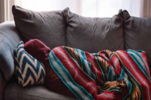 A sick person lying under a blanket on the couch