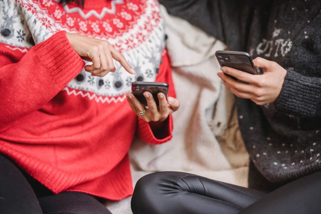A shot of two phones held by people in Christmas sweaters.