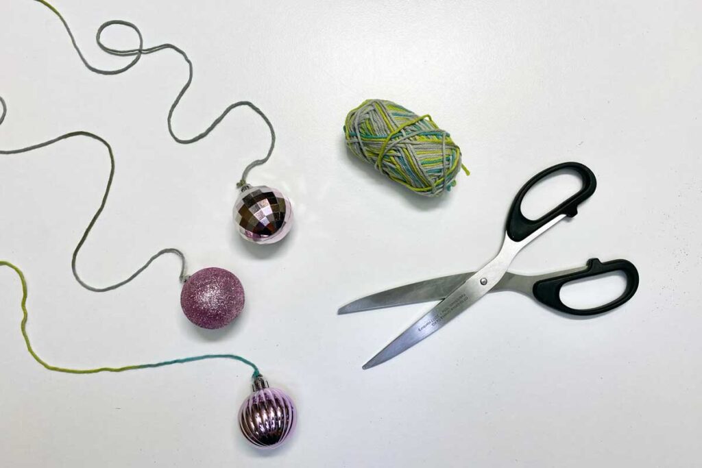 Three Christmas baubles attached to string lying next to the roll of string and scissors