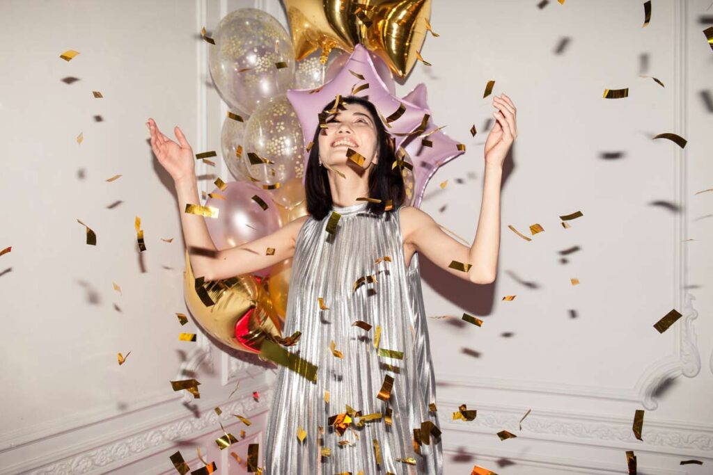 A woman dressed in a sparkly dress celebrates with confetti and balloons during a New Year photo shoot
