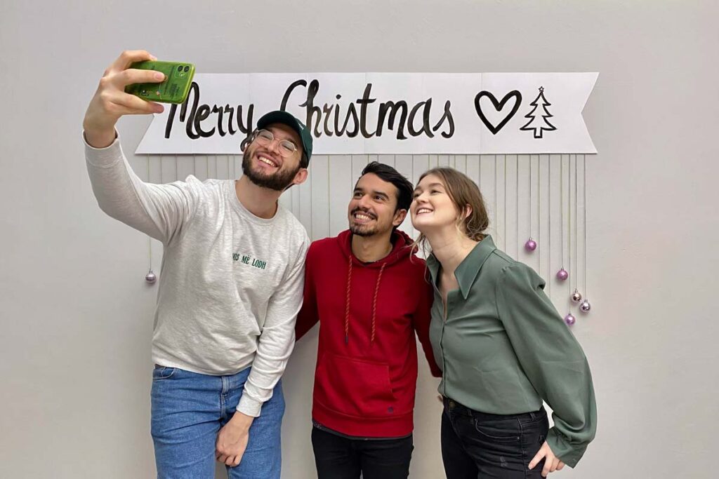 Three people pose in front of the DIY Christmas photo booth for a selfie.